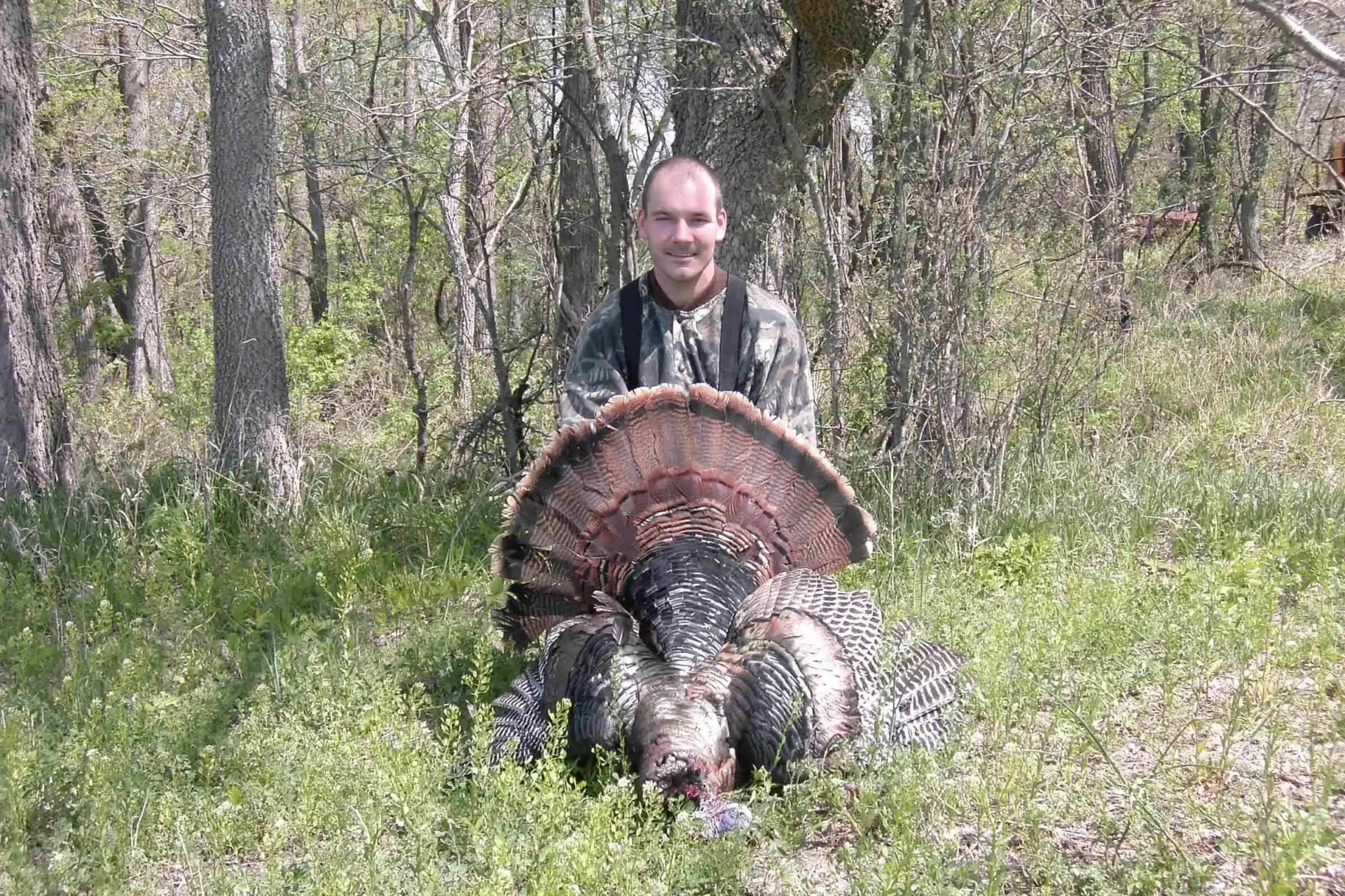 A man sitting next to a turkey in the woods.
