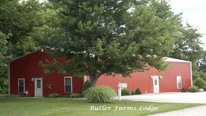 A red barn with trees and bushes in front of it.