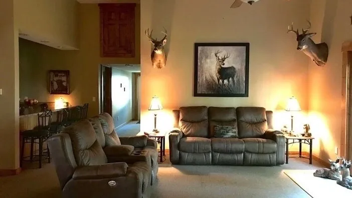 A living room with couches and chairs, a table and a deer head.