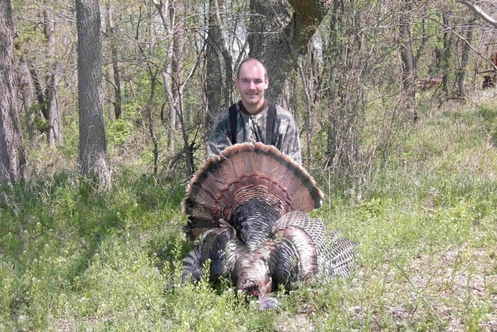 A man poses with his turkey in the woods.