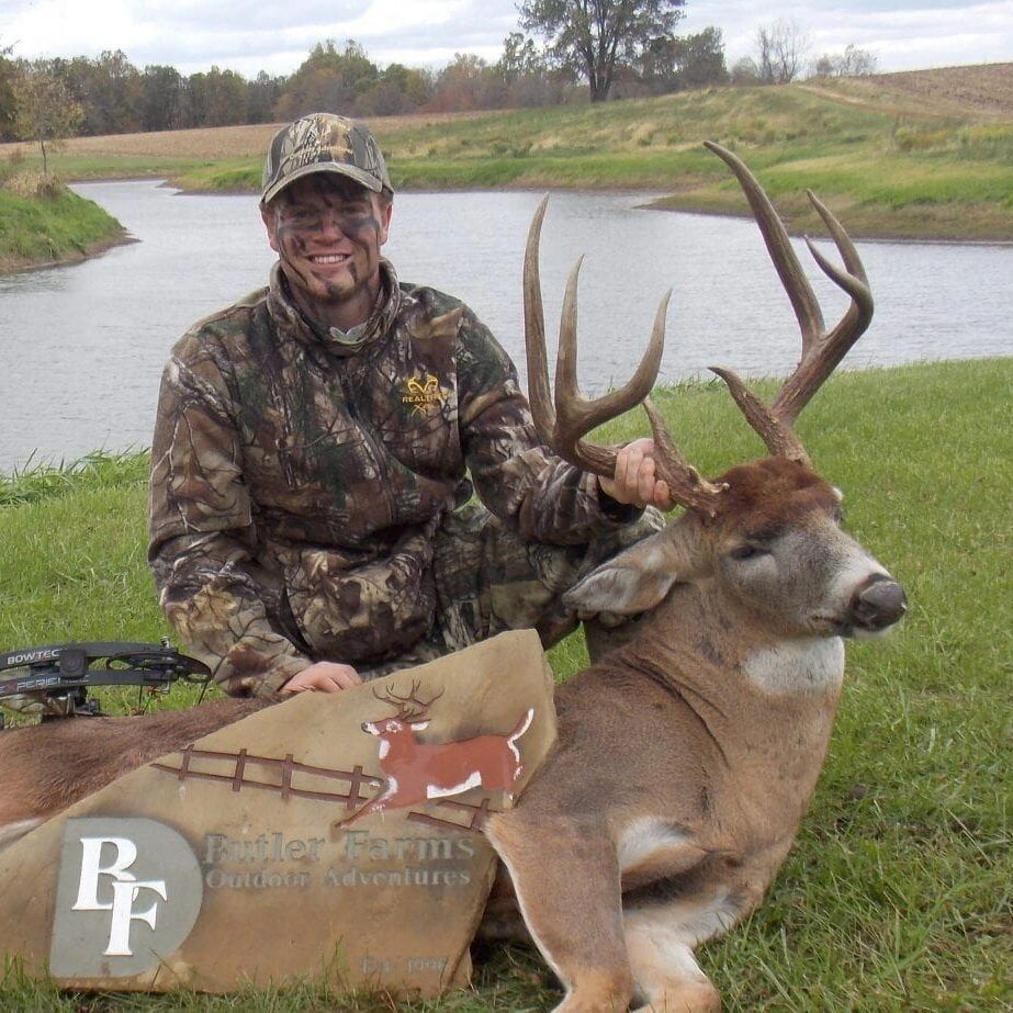 A man in camouflage sitting next to a large deer.